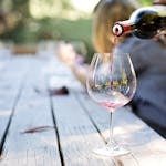 A hand pouring red wine into a glass on an outdoor table, creating a relaxed atmosphere.