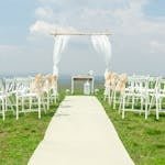 Elegant outdoor wedding setup with chairs and arch under a blue sky.