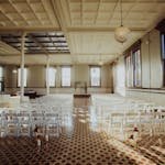 Spacious and elegant indoor wedding venue adorned with chairs and chandeliers, ready for a ceremony.